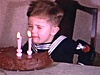 Enfant habillé en matelot qui tente de souffler les 3 bougies de son gâteau d'anniversaire