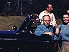 Belle automobile décapotable avec une belle femme en chandail bleu qui pose devant (prennent un verre); son auto