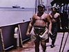 Sur le pont d'un navire, marins torse nu au travail, mer houleuse et vagues qui montent sur le pont