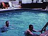 Autour de la piscine du motel (Floride): chaises Adirondack colorées, un des deux hommes embrasse sa femme assise au bord de la piscine