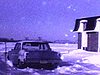 Auto stationnée au bord d'un champ enneigé, près d'un bungalow années 70