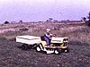 Beau plan d'un garçonnet qui conduit un tracteur à gazon avec remorque, la caméra le suit bien autour du bungalow et des bâtiments