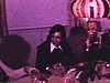 Dames autour de la table qui jasent en fumant et écoutent la télévision (mode très laide des années 70 dans une réunion de famille au salon)