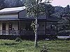 Maison de campagne (chalet) avec quelques personnes sur la galerie et l'automobile stationnée tout près; puis, les alentours de la maison en panoramique