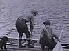 Deux hommes partent en canot sur le lac.  Puis un autre en chaloupe; paysage boisé, 
