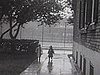 Années 20; Les deux enfants, sous la pluie, en imperméables avec chapeau, dans la cour de la maison; ils traînent un gros voillier jouet qu'on voit ensuite dans un bassin avec fontaine (très beaux plans)