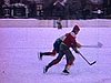 Extérieur / hiver; enfant emmitoufflé sur le bord de la bande de la patinoire; hockey avec uniformes en ville
