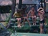 Camping - beau plan de 4 enfants assis à la table à pique-nique devant la tente-roulotte. Maman fait des grimaces