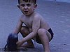 Années 50: garçonnet à la plage joue dans le sable avec un petit seau, boardwalk, des enfants se croisent et se saluent