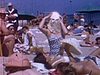 Beaux plans de filles qui se font bronzer étendues sur la plage; une fille porte son chapeau comme un masque; plage très achalandée
