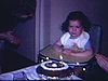 Bébé fille dans sa chaise haute devant son gâteau d'anniversaire de 2 ans. Maman tape des mains en chantant, petite applaudit énergiquement