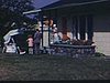 Sur le terrain d'un chalet à Rivière-du-Loup, famille en visite une autre. Vieux monsieur aveugle sur une balançoire, on jase puis la famille pose devant le chalet