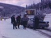 Plusieurs autos stationnées en file au bord d'une route isolée enneigée en forêt. Des ami(e)s.Les hommes se sont arrêtés prendre un coup  de gin à même la bouteille (boisson)
