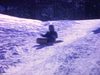 Enfant dans une luge glisse à l'extérieur (hiver) descent la côte et remonte avec son traineau puis redescend