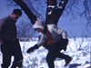 Monsieur et madame en hiver avec leur chien qui grimpe dans l'arbre. Madame glisse en ski, monsieur nettoie ses bottes pleine de neige avec un balai