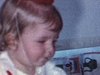 Bébé fille devant son gâteau à 1 bougie. Elle tient un billet de 2 dollars à la main et devant elle, ses cadeaux