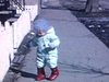 Printemps: sur la rue en ville, bébé fille marche habillée en habit d'hiver