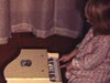 Fillette joue du piano jouet.  On voit un disque de Jacques Aleystock sur le tourne-disque