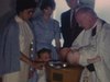 Baptême à l'église (cérémonie) Le prêtre attendri prend le bébé dans ses bras. Le petit frère s'impose un peu devant la caméra. Maman prend bébé