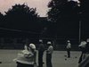 Plusieurs plans de nombreux hommes qui jouent à un jeu de boules sur un terrain aménagé avec estrade et public. Un jeu qui semble à mi-chemin entre les quilles et la pétanque.