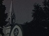 Église, puis route de campagne en terre et petite maision en pièce sur pièce recouverte de chaux.