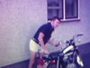 Un homme enfourche sa moto et prend différentes poses pour la caméra, suivi d'un jeune homme aux cheveux longs.