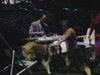 Pique-nique sur table, chien colley, dans la cour du chalet, au bord d'un court de tennis. Femmes jouent au tennis sous le regard de la famille