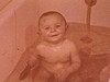 Bébé fille dans son bain joue avec jouet flottant, maman lave bébé