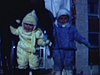 Bébé emmitouflé près d'une statue du bonhomme carnaval, la mère amene un autre bébé et ils saluent la caméra