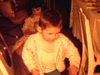 Enfants jouent par terre dans la cuisine, petite fille avec poupée elle va la coucher dans un petit lit, garçon avec tracteur, adultes discutent au salon, les enfants mettent leur pyjama