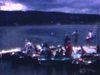 Foule entassée sur un quai de lac, des chaloupes accostées (plan bref et un peu sombre)