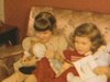 Deux petites filles assises en belles robes sur le divan au salon, elles tiennent des poupées, se couchent sur le dos et lèvent les jambes en l’air
