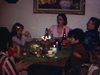 Anniversaire d’une fillette, souper à la salle à manger, une femme éloigne les bouteilles de vin pour que la petite puisse souffler ses bougies, petite soeur dans chaise haute souffle aussi un gâteau à une bougie