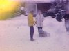 Famille à l’extérieur de la maison l’hiver, bébé emmitouflé dans un traineau, 2 hommes vont fouiller dans la neige et sortent des débris pour les montrer à la caméra