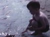 Garçon au bord de l’eau sur la plage avec des petits bateaux en plastique