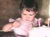 Anniversaire d’une petite fille de 2 ans, elle souffle sur ses bougies, enfants autour de la table mangent le gâteau, adultes debout à la cuisine les regardent