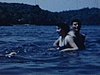 Des gens se baignent dans un lac et essaient de monter dans une chaloupe