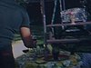 Un homme prend un verre sur la table extérieur de la cour de la maison, un jeune homme roule le fil de la tondeuse, une jeune femme en robe d’été est avec eux