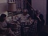 Anniversaire d’un homme âgé, famille au salon, un enfant sur ses genoux, il reçoit une montre, du vin, un collier. une femme apporte un gâteau plein de bougies allumées, il souffle et tout le monde applaudit