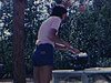 Une femme fait à manger sur un poêle à gaz à l’extérieur, une petite fille en maillot de bain va chercher une bière à l’intérieur de la maison mobile, une femme boit sur une chaise longue, en fumant - camping