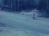 Une fille en jaquette se promène en bicyclette sur un chemin de terre, un homme en motocyclette à côté d’elle