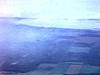 Panorama du haut d’une montagne sur des champs et collines, une femme les bras croisés, marche sur le bord de la route qui mène à un bungalow