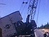 Sur le bord de la route, un camion de déménagement au pare-choc accidenté. inscription Monving inc.Déménagement du golf», accroché à une grue, hommes à casque de travail regardent