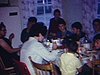 La famille est assise à table et mange, une femme les sert et une petite fille regarde la caméra