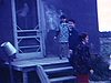 Une famille en habit sort d'une automobile et monte des escalier pour entrer dans la maison, une femme salut la caméra