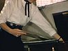 Une femme avec des lunettes et un bel habit met un disque vinyl dans le tourne-disque du salon, un petit garçon en habit de hockey du Canadien avec ses patins et son bâton à l’intérieur