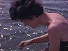 Une femme se brosse les dents dans l’eau du lac, un homme en serviette se lave le visage, famille dans un canot se lave - camping