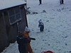 Des enfants en habits d’hiver jouent dans la première neige, ils tirent un bébé dans un traineau sur le terrain du bungalow