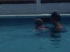 Un homme dans une piscine au bord de la mer montre à une fillette à nager