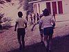 Des enfants marchent vers une toilette publique sur un terrain à l’extérieur, ils essaient de grimper sur la parois d’une falaise